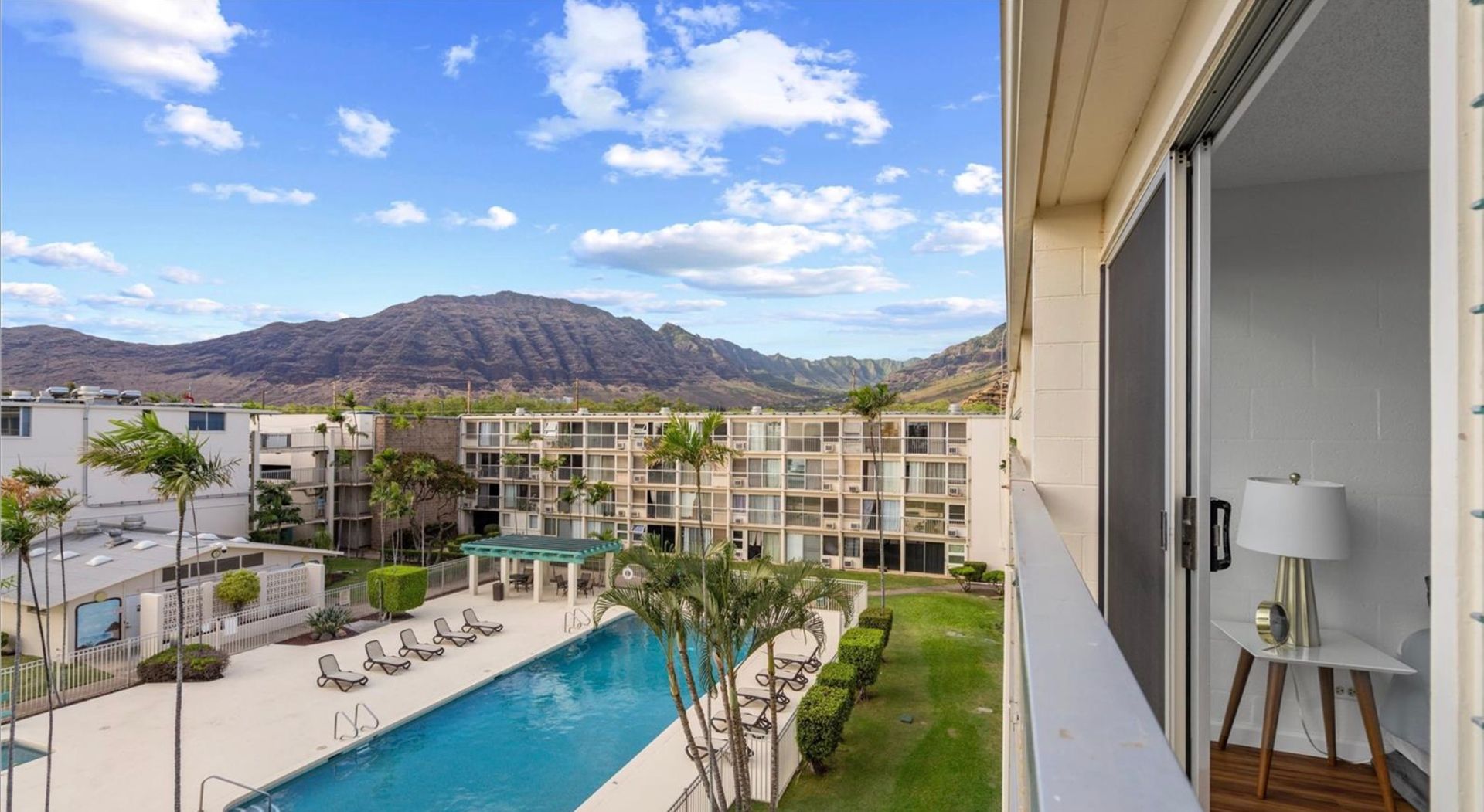 A view of a swimming pool from a balcony with mountains in the background.