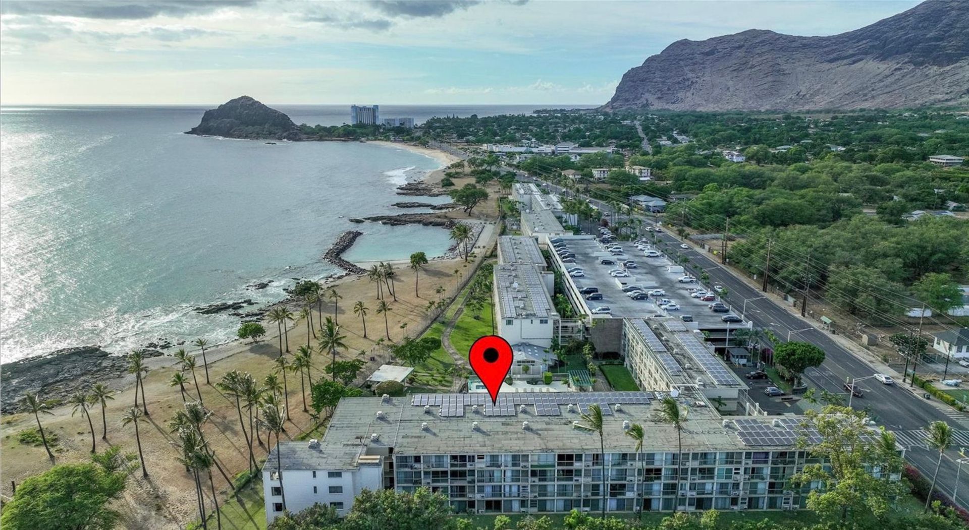 An aerial view of a building next to the ocean and a mountain.