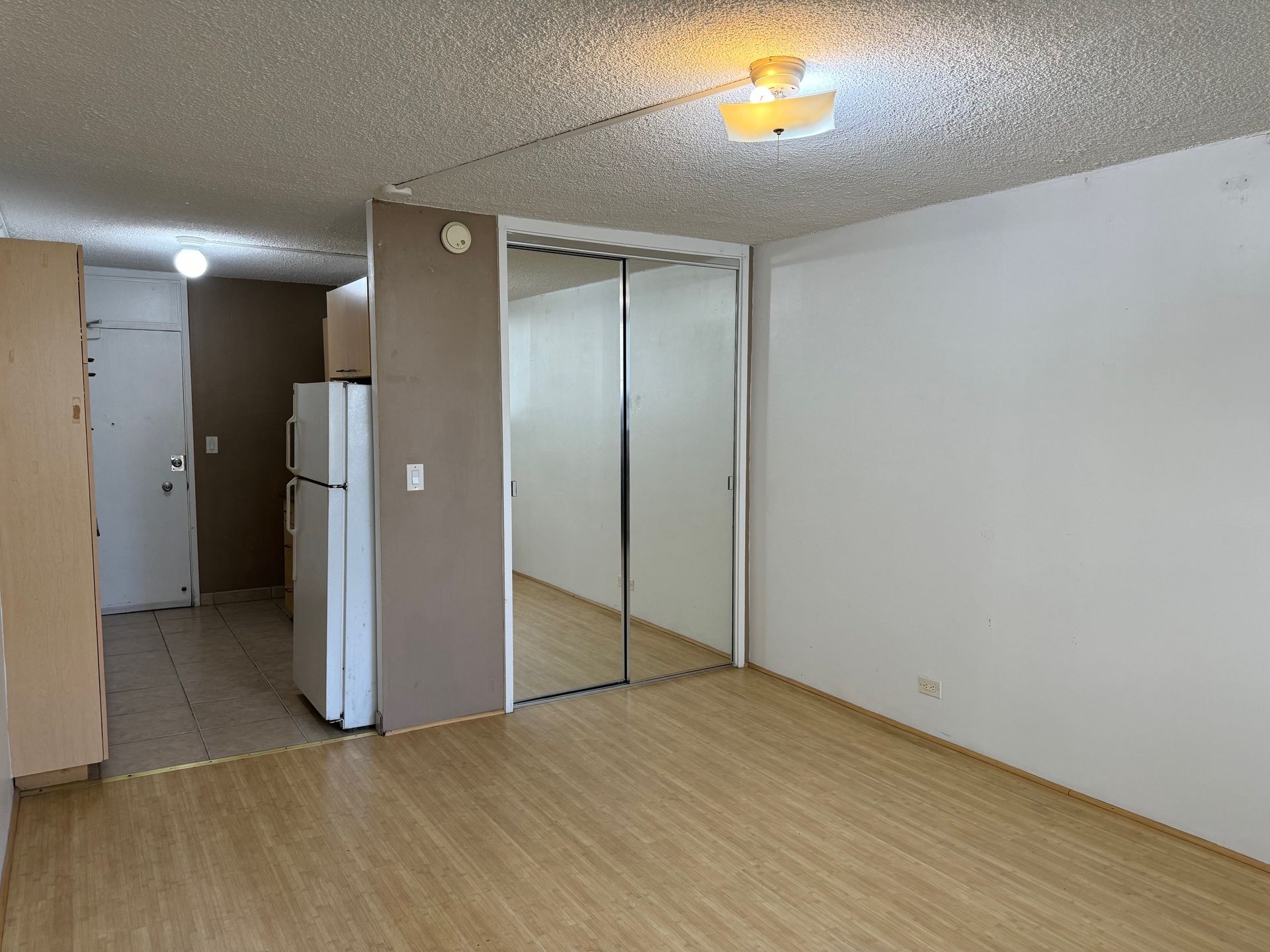 A living room with a refrigerator and a mirrored closet.
