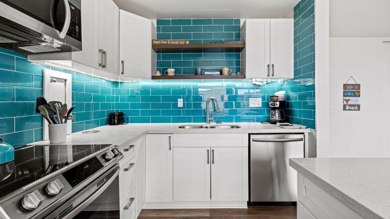 A kitchen with white cabinets , stainless steel appliances , and blue tiles.