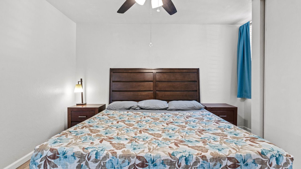 A bedroom with a bed , nightstand , lamp and ceiling fan.