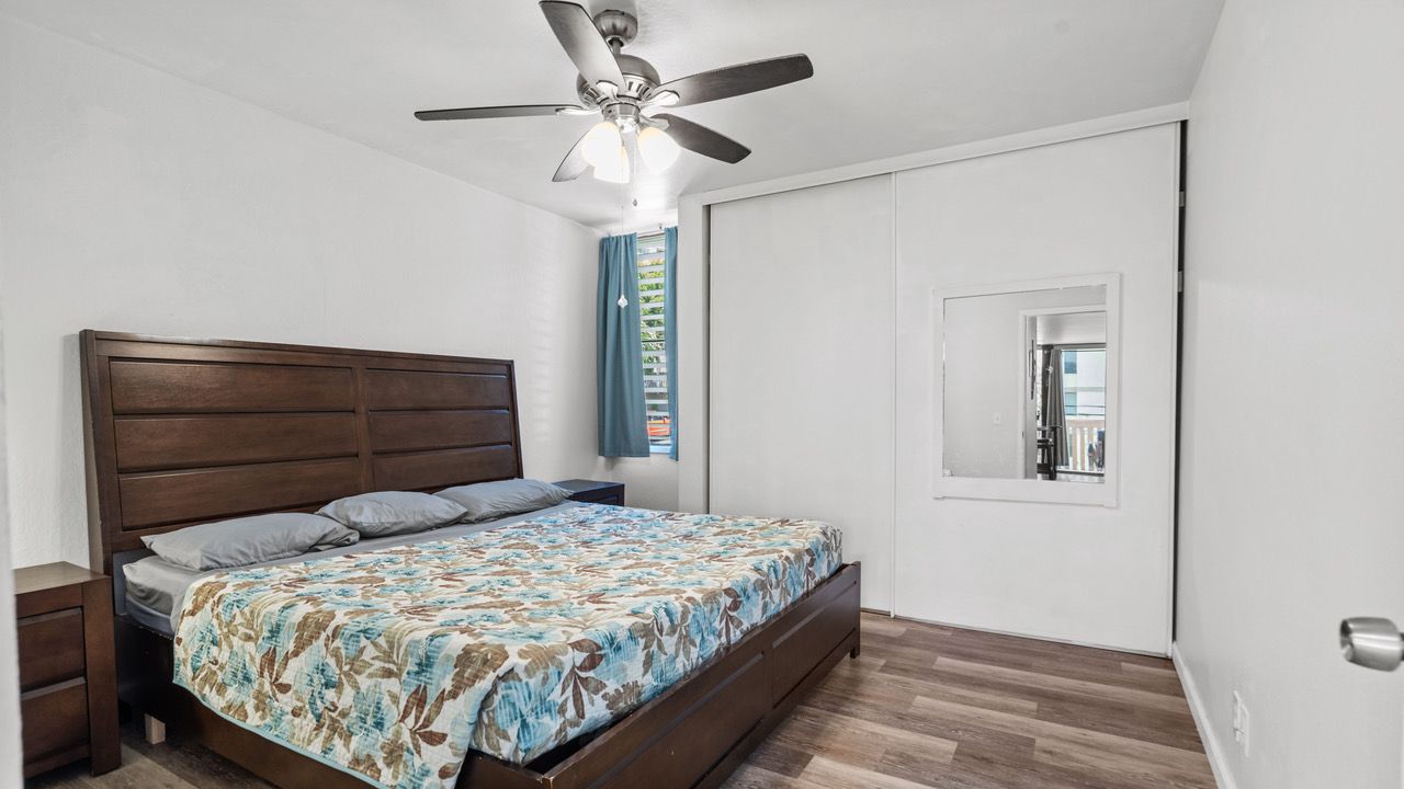 A bedroom with a bed , nightstand , mirror and ceiling fan.