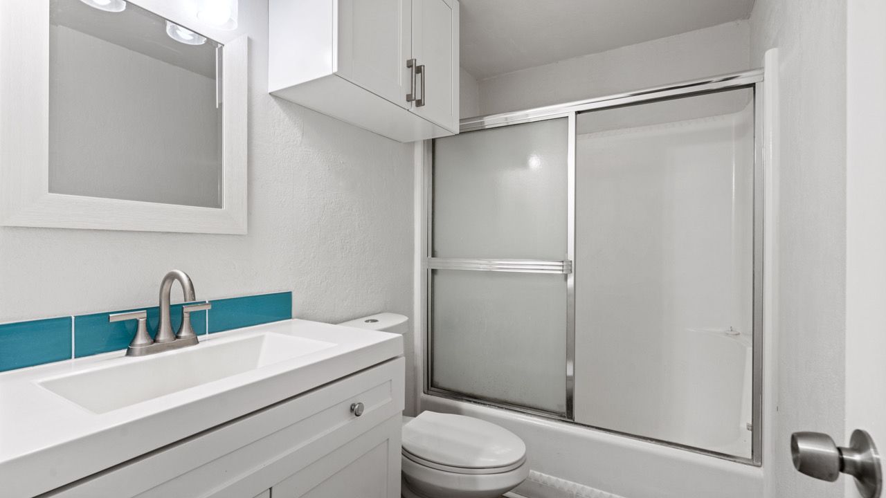 A bathroom with a sink , toilet , shower and mirror.