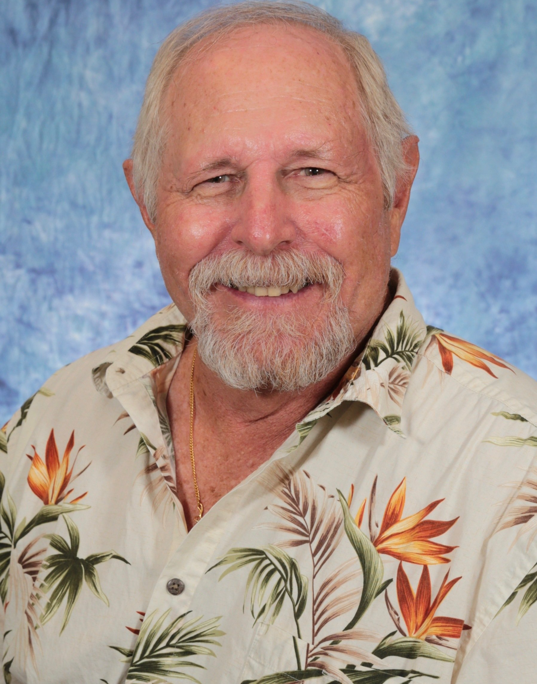 A man with a beard is wearing a hawaiian shirt and smiling