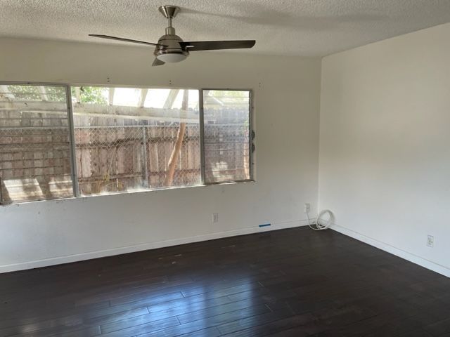 An empty living room with a ceiling fan and a large window.