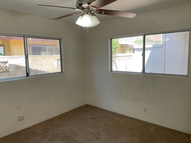 An empty room with a ceiling fan and two windows