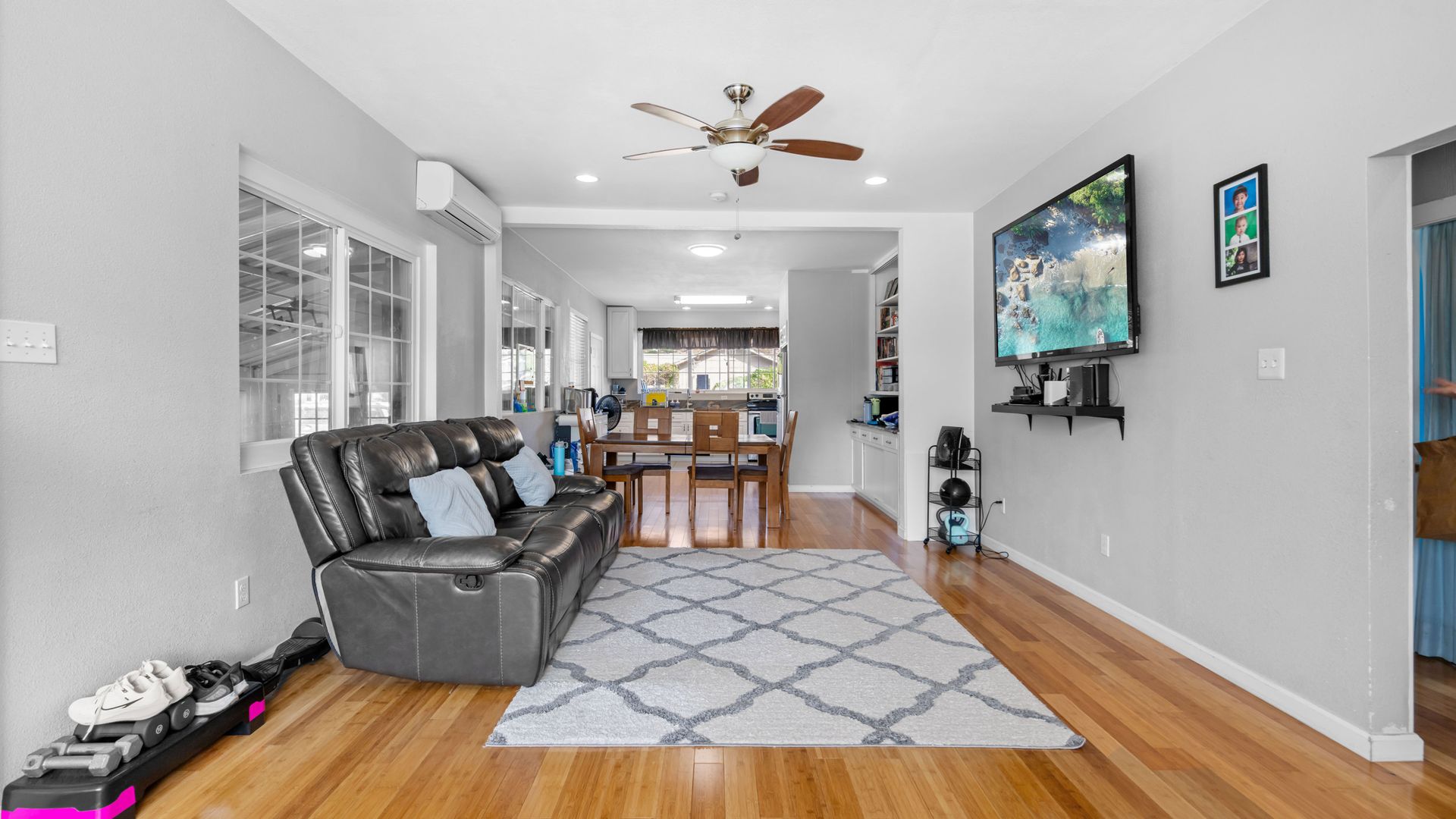 A living room with hardwood floors , a couch , a television and a ceiling fan.