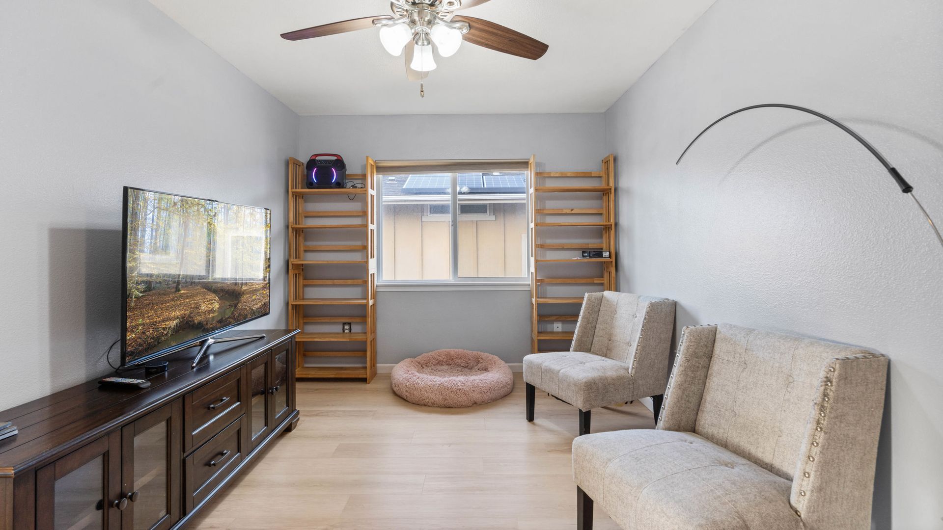 A living room with a television , chairs , a dog bed and a ceiling fan.