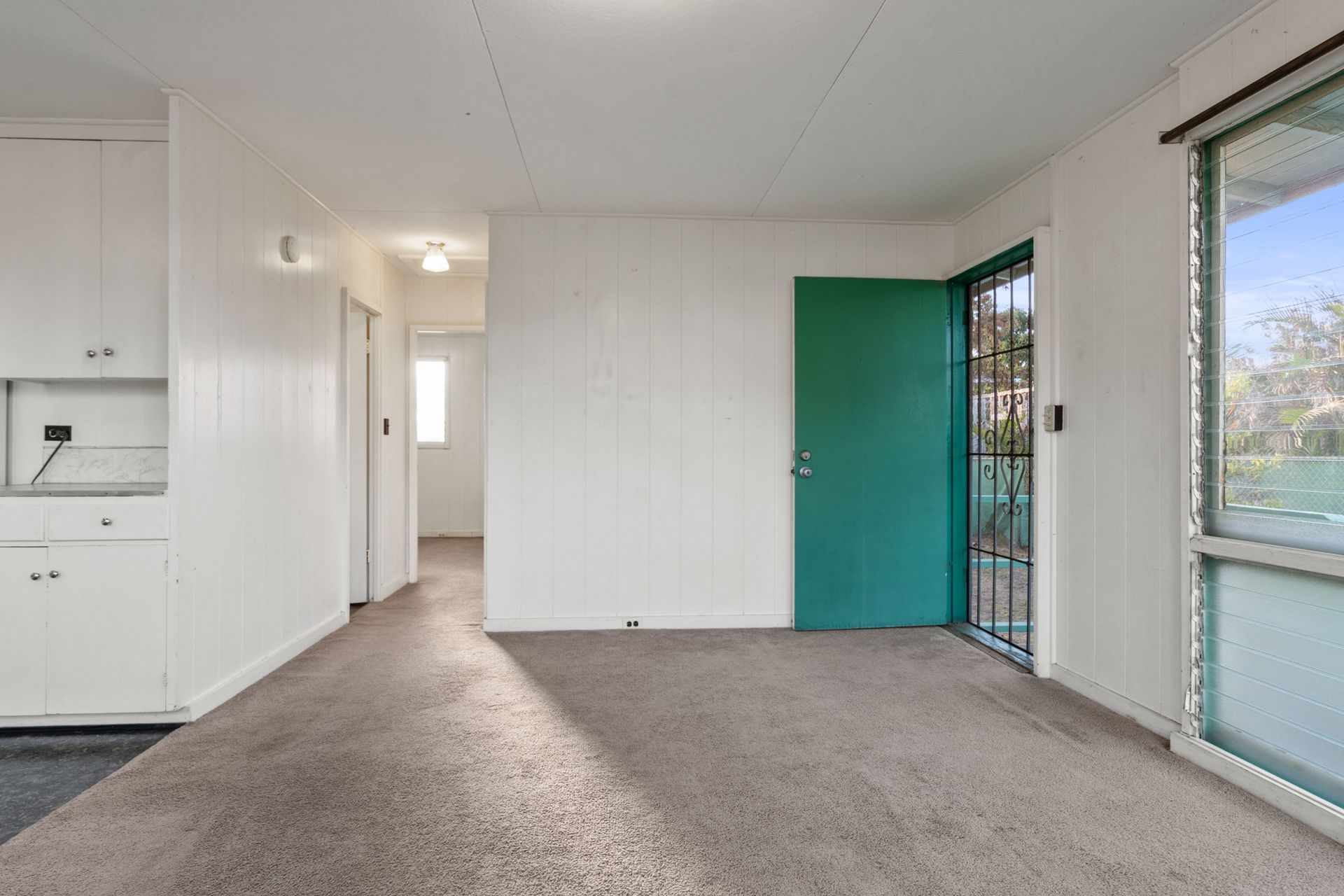 An empty living room with a green door and a window.