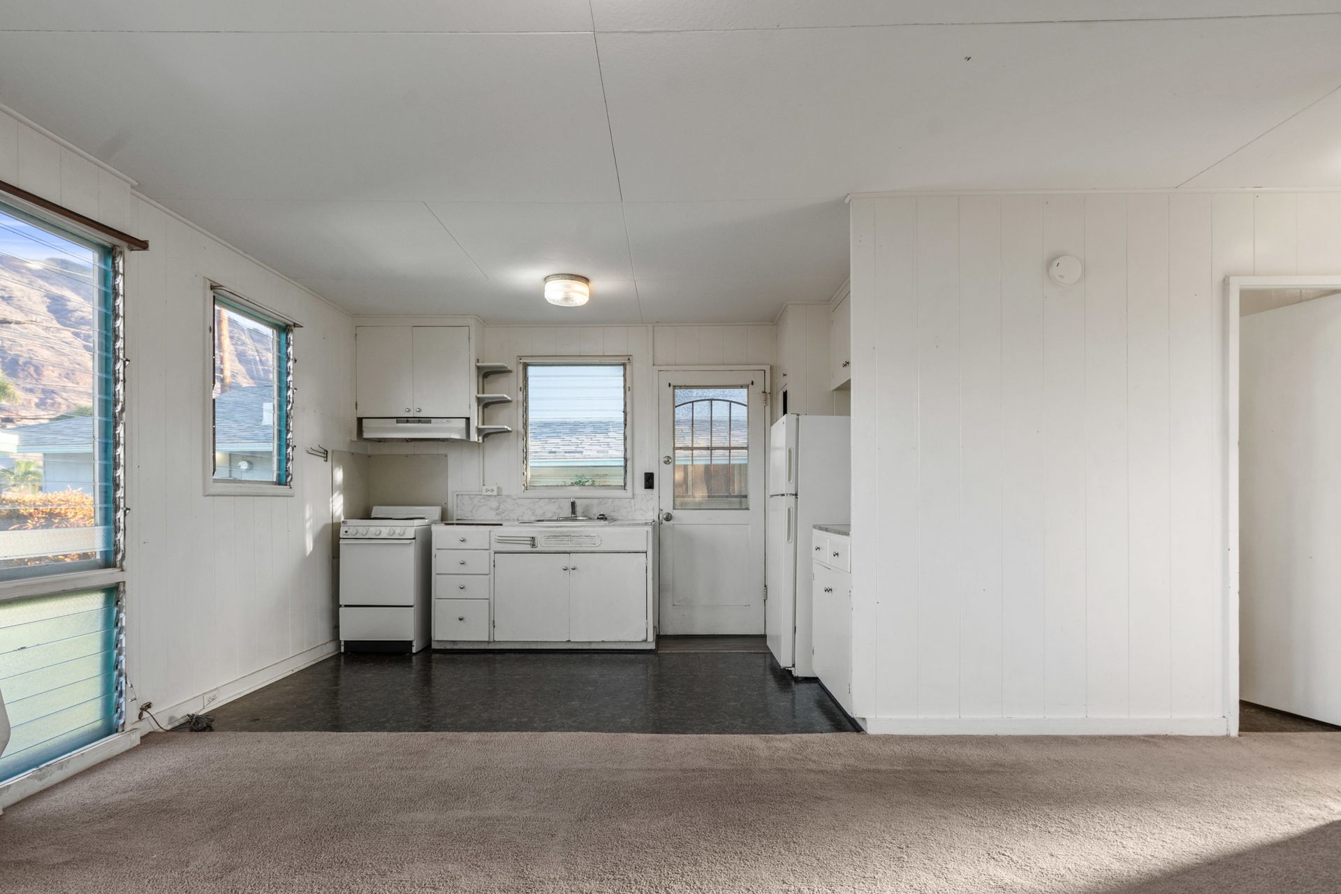 An empty kitchen with white cabinets and a refrigerator