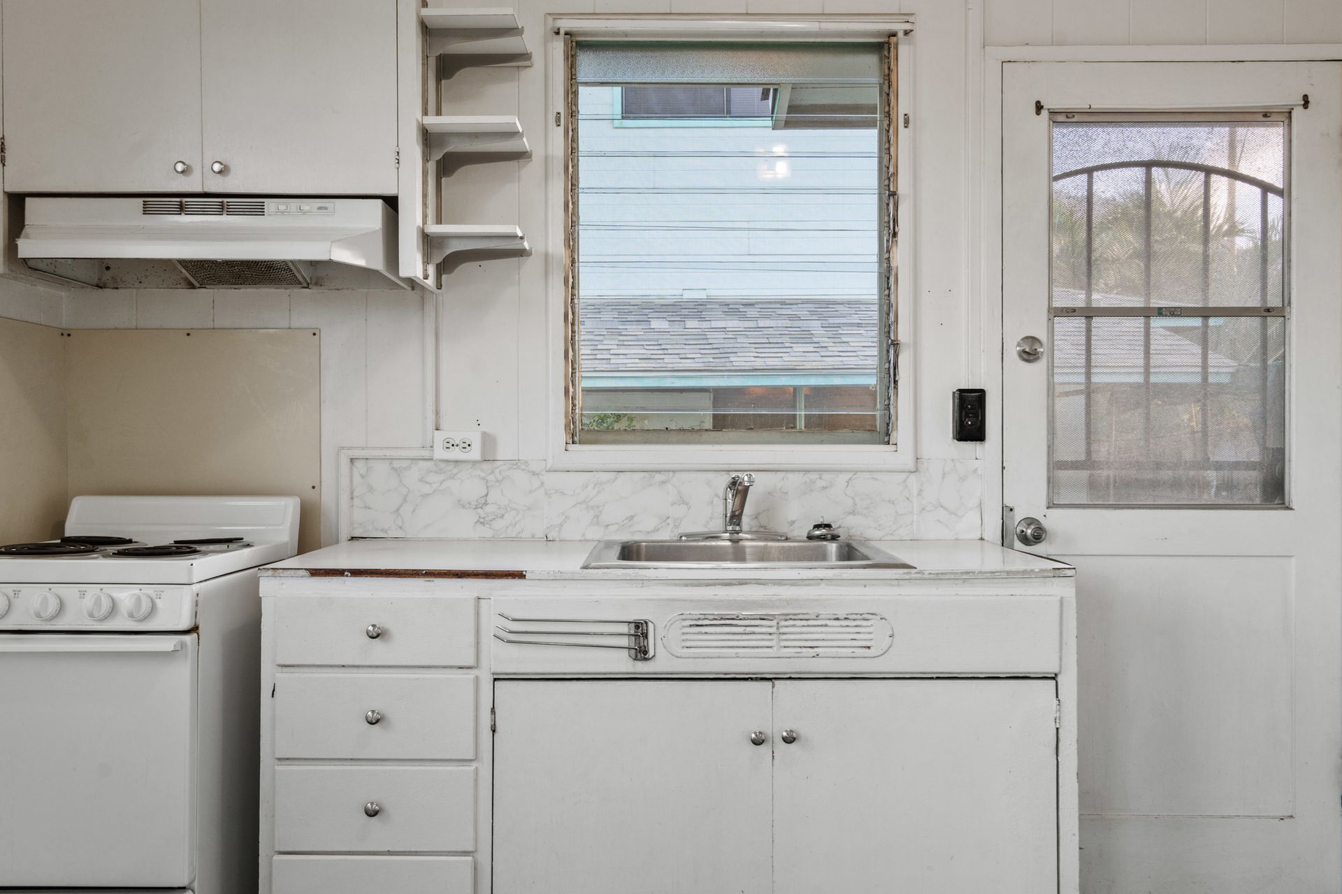 A kitchen with white cabinets , a stove , a sink and a window.