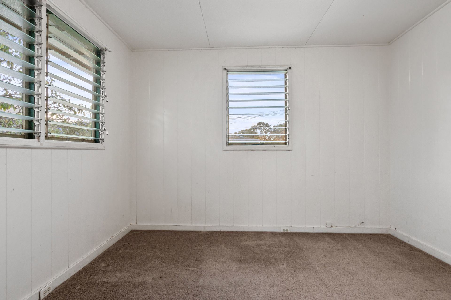 An empty room with a window and a brown carpet.