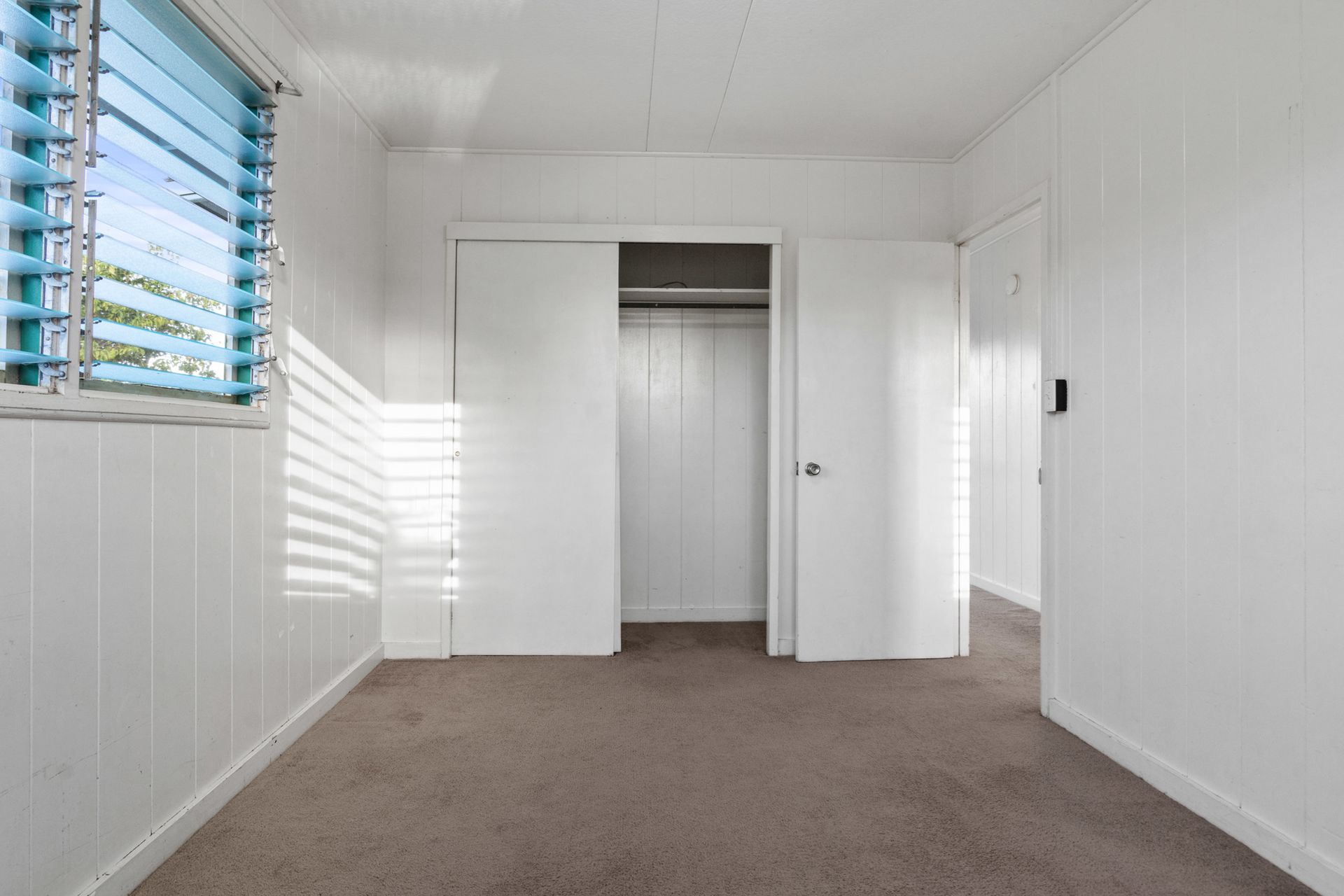 An empty bedroom with a closet and a window.