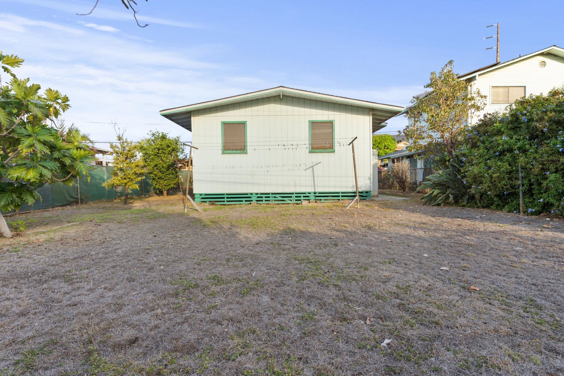 A small green house is sitting in the middle of a dirt field.