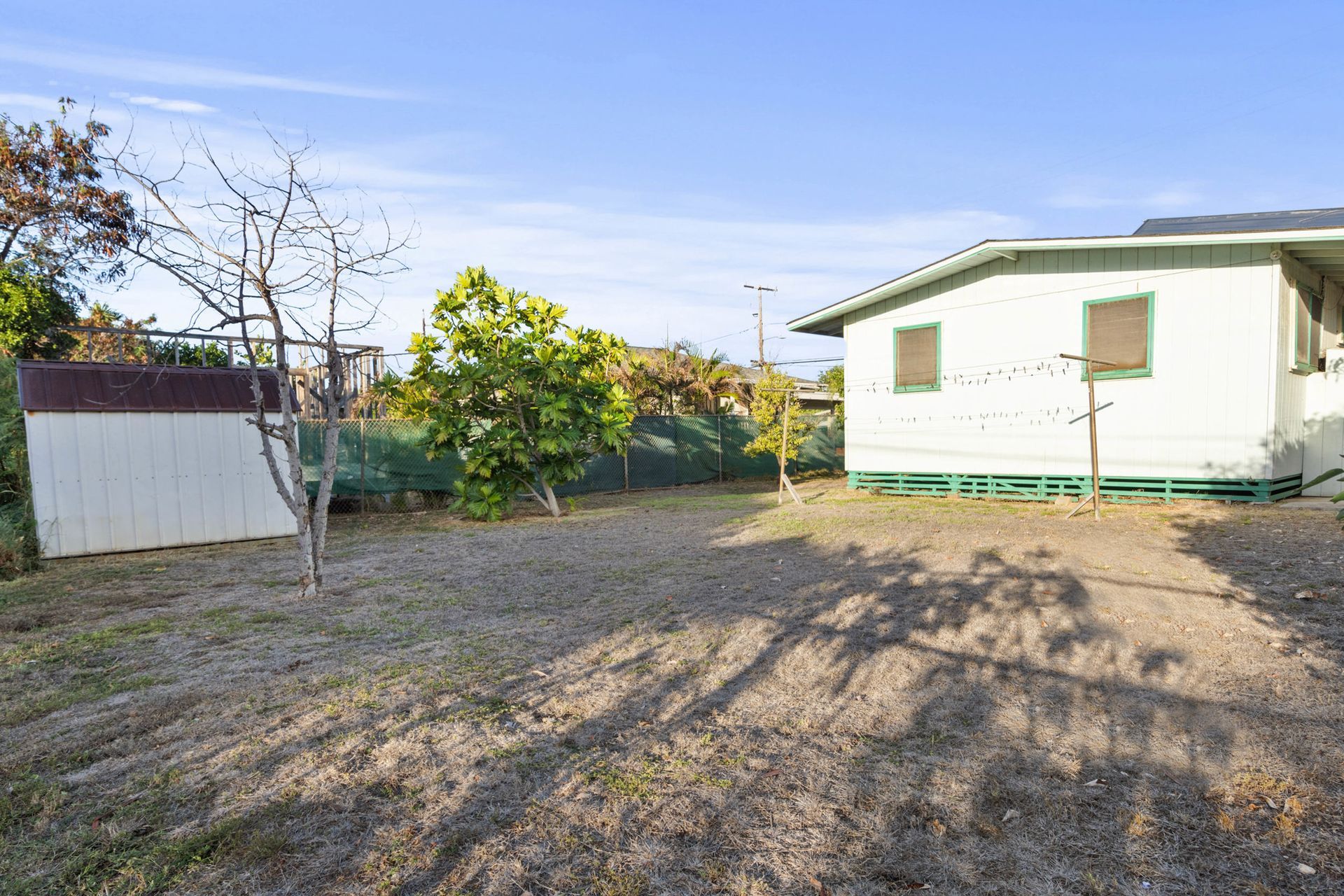 A white house with a green roof is sitting in the middle of a dirt field.