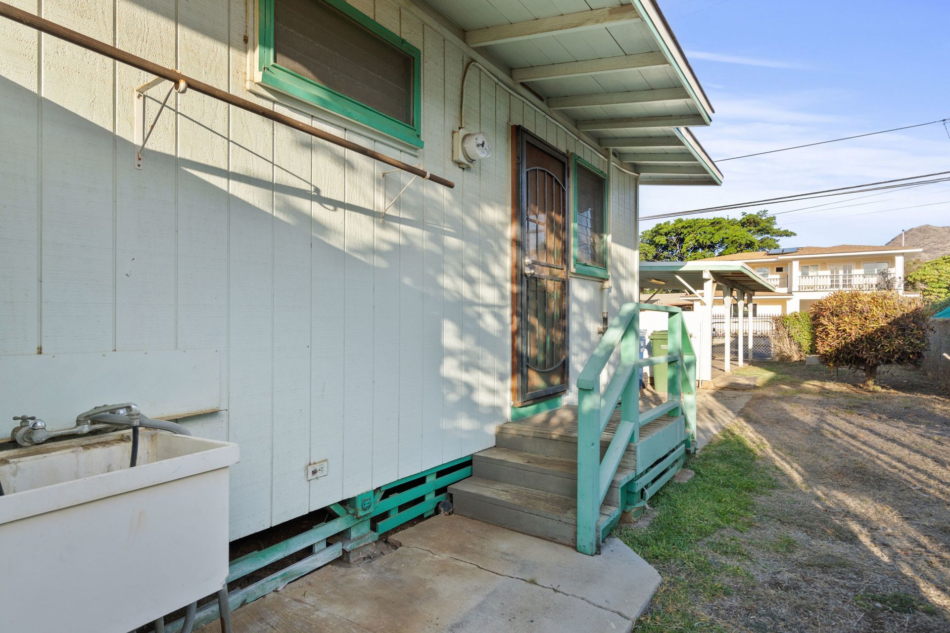 A white house with green trim and a sink in front of it.