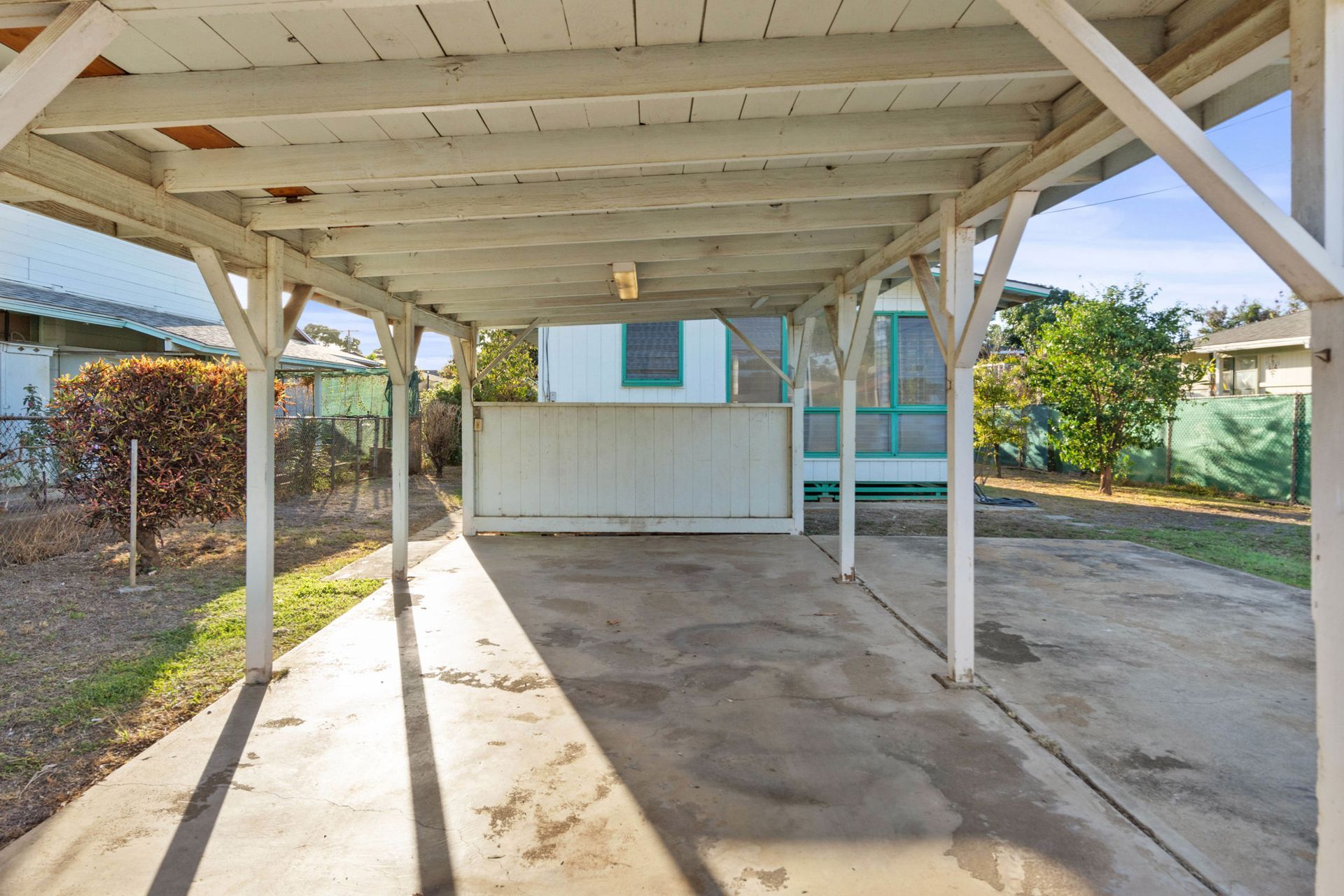 A carport with a wooden roof and a concrete floor in front of a house.