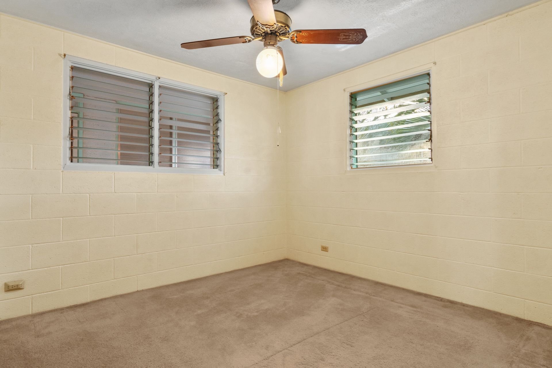 An empty bedroom with a ceiling fan and two windows.