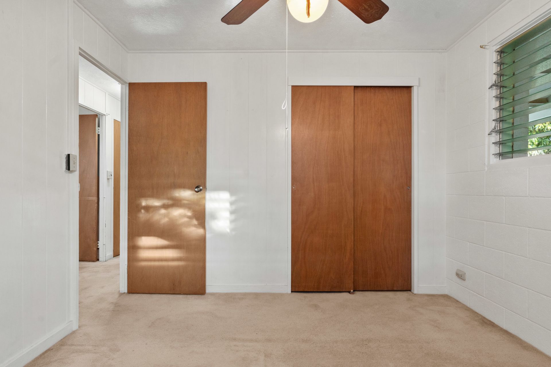 An empty bedroom with two wooden doors and a ceiling fan.