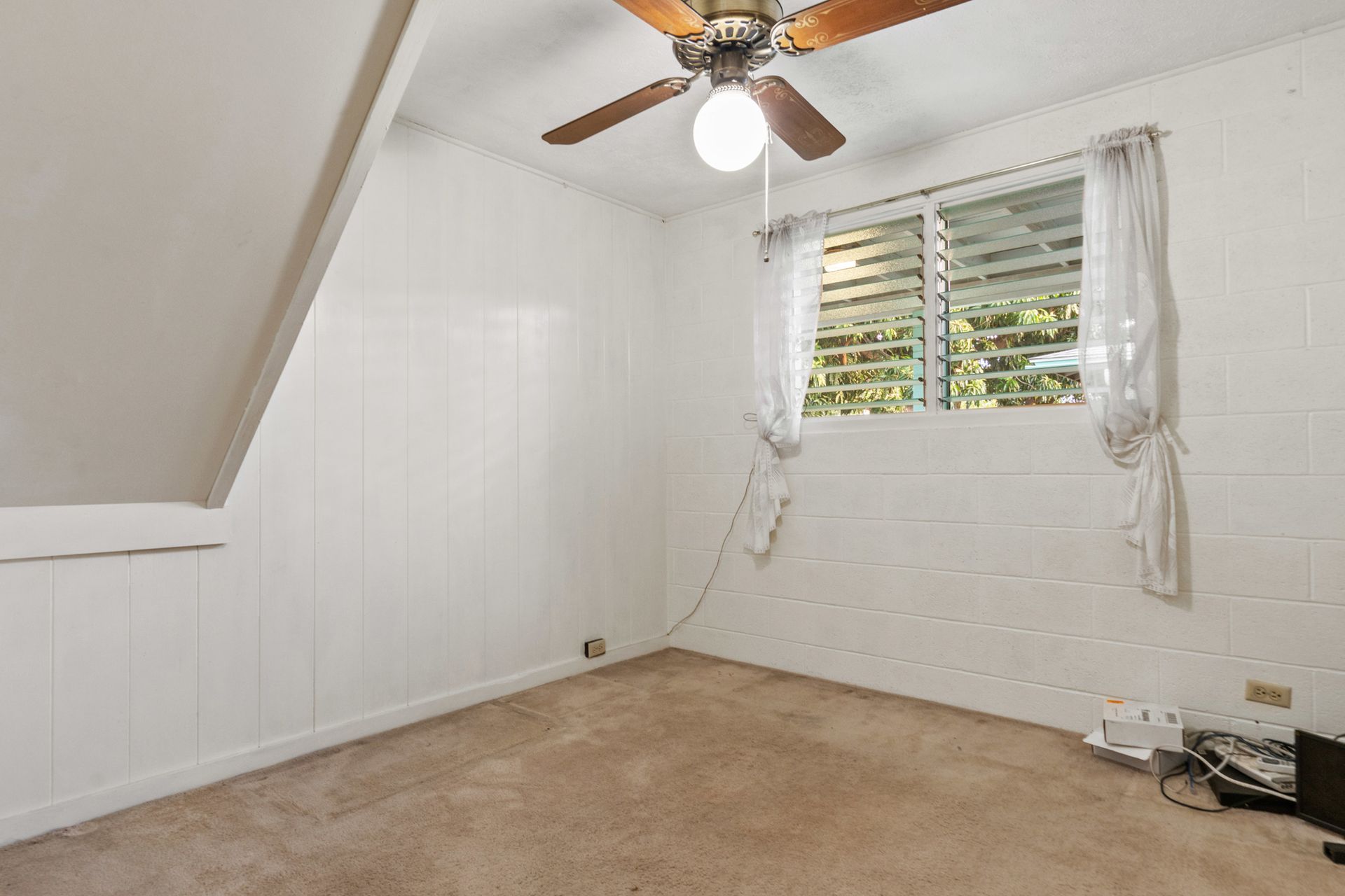 An empty room with a ceiling fan and a window.