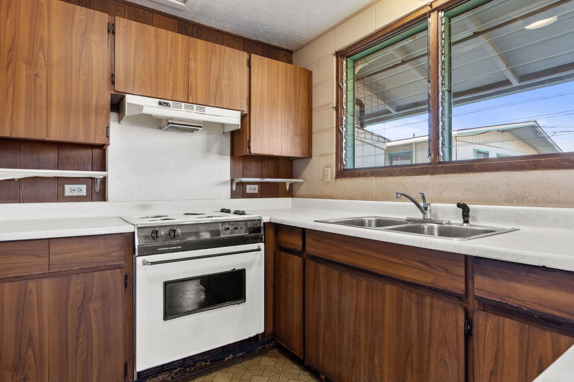 A kitchen with wooden cabinets , a white stove , a sink and a window.