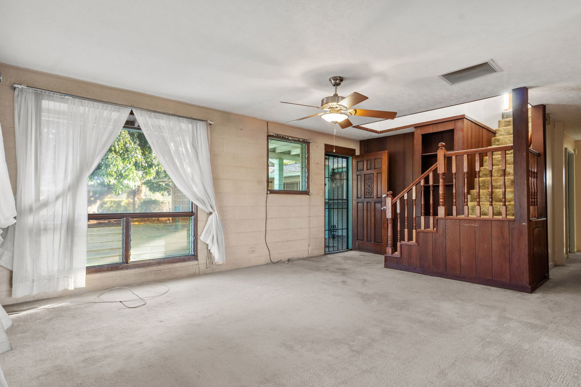 An empty living room with a ceiling fan and stairs.