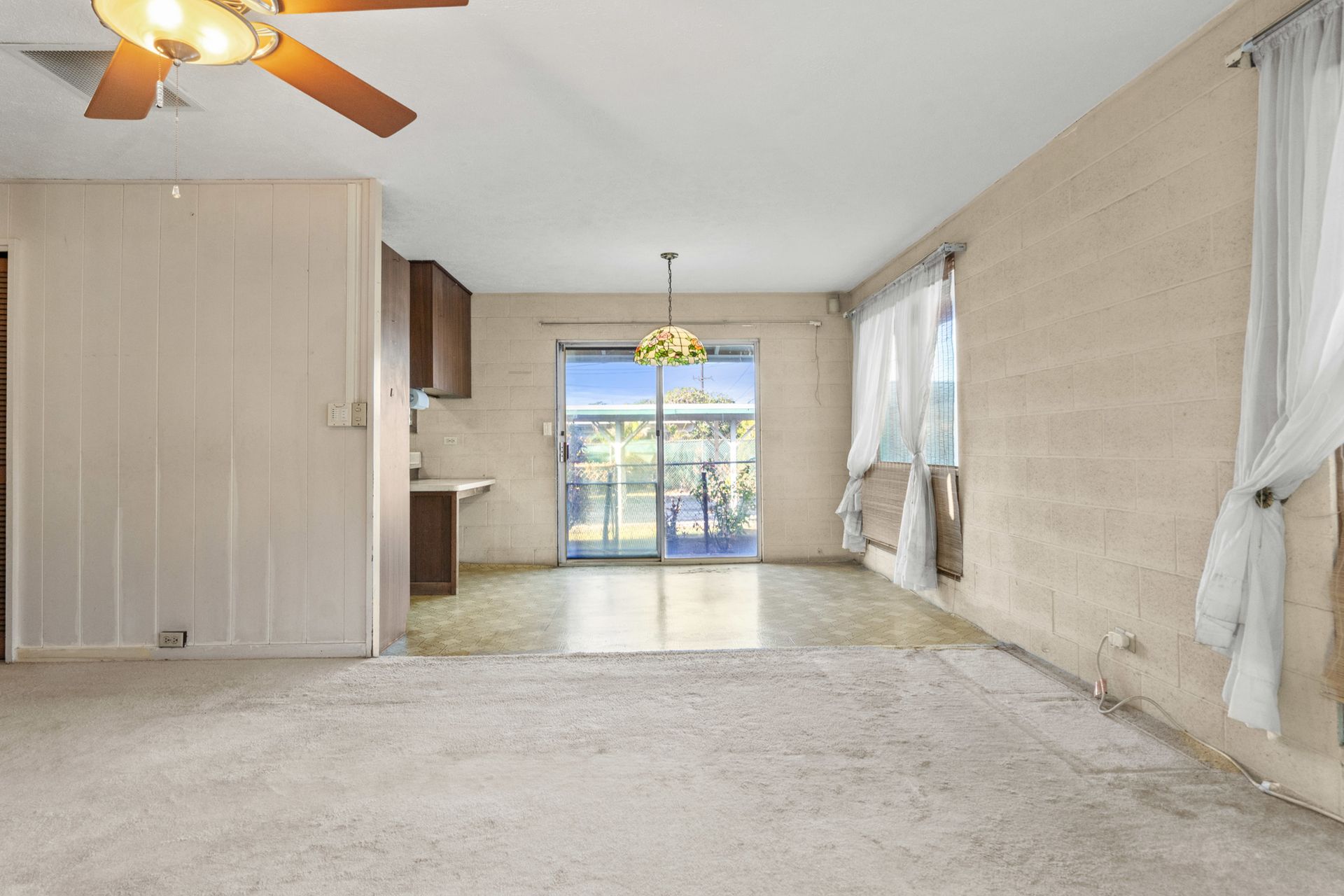 An empty living room with a ceiling fan and a sliding glass door.
