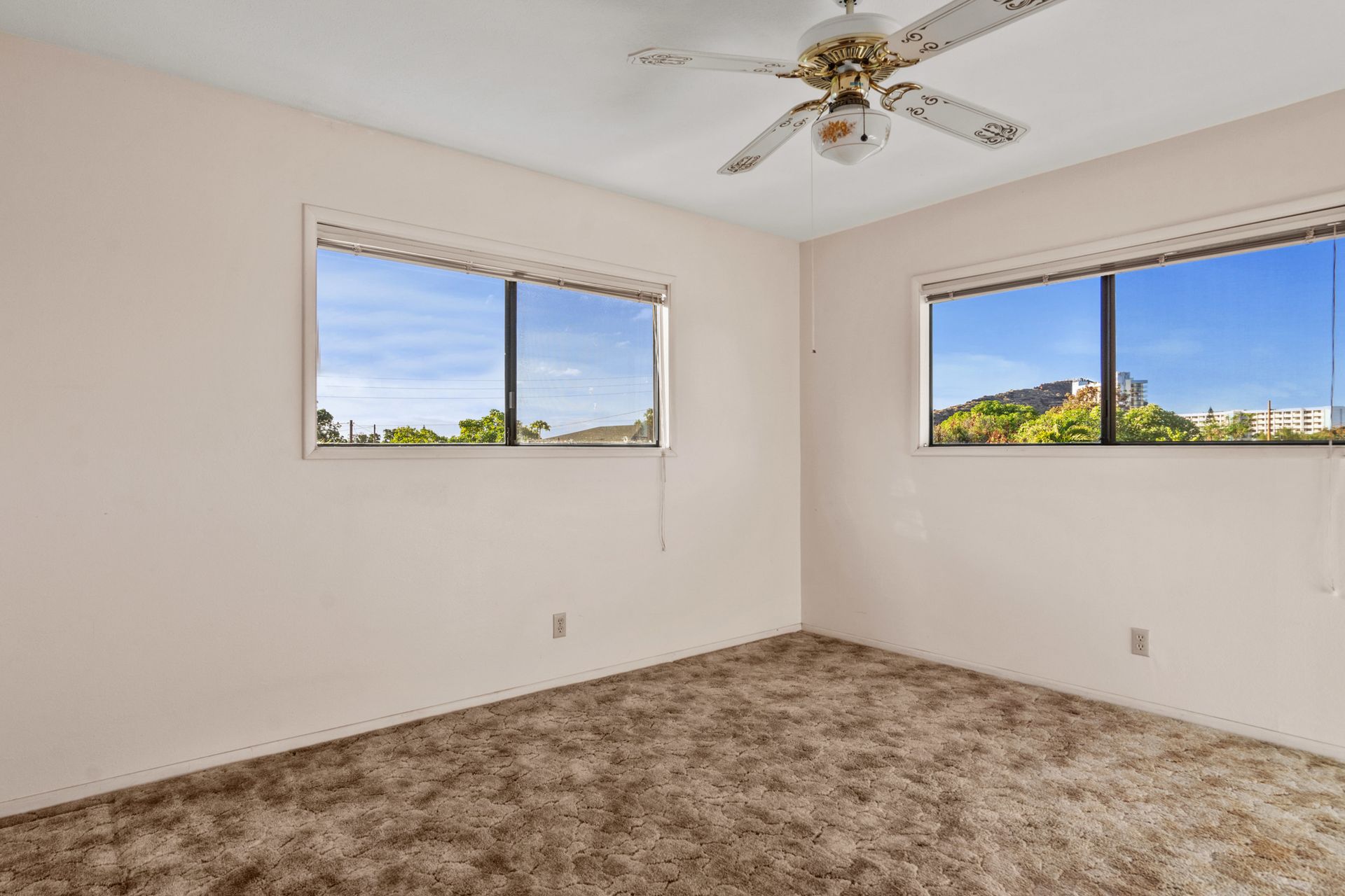 An empty bedroom with a ceiling fan and two windows.