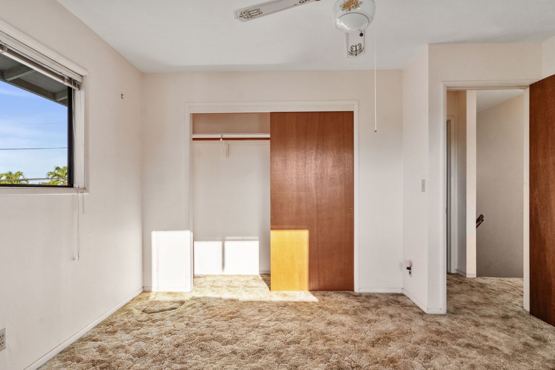 An empty room with a window and a ceiling fan.