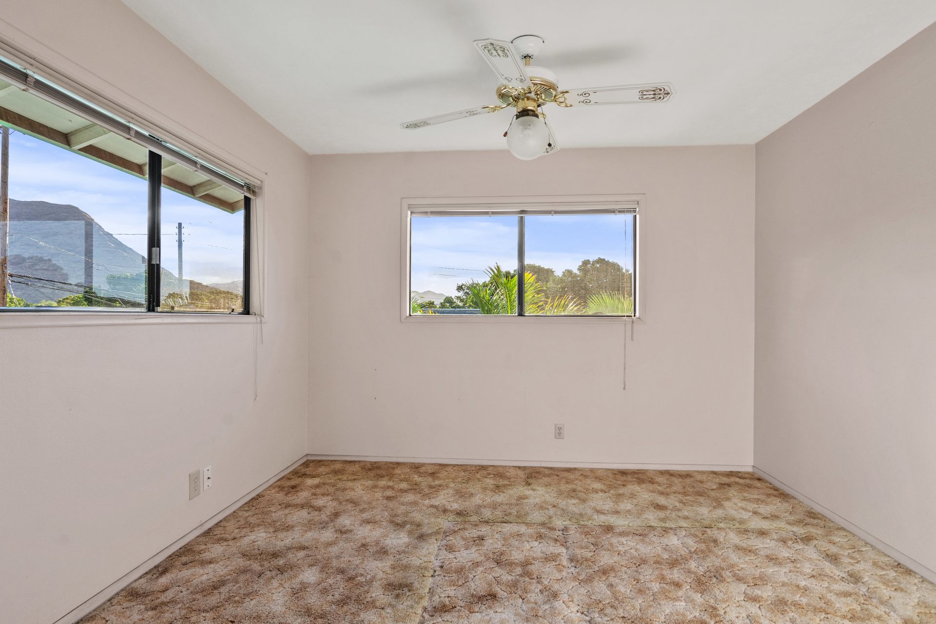An empty room with a ceiling fan and two windows