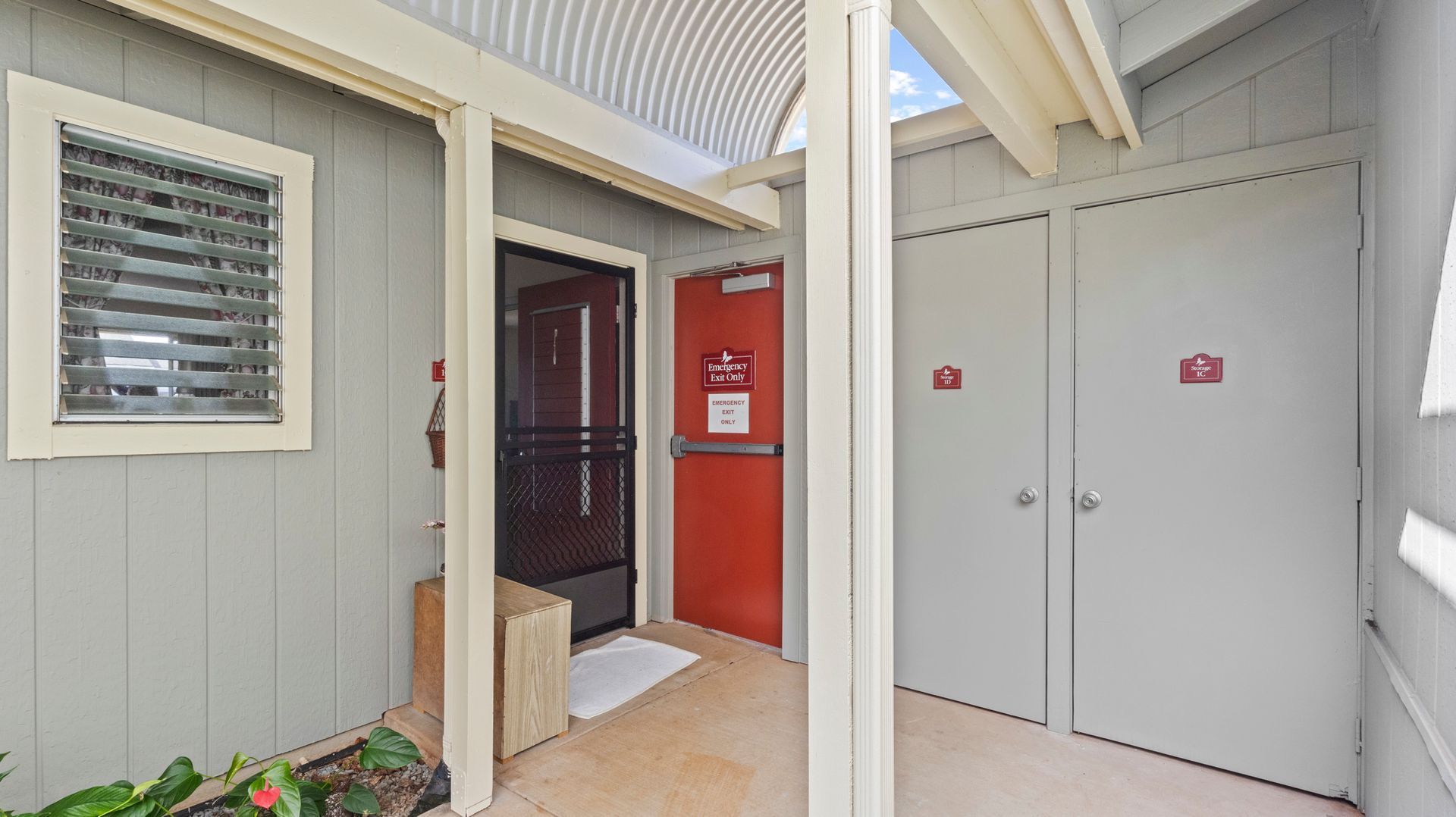 There is a red door in the middle of a hallway between two buildings.