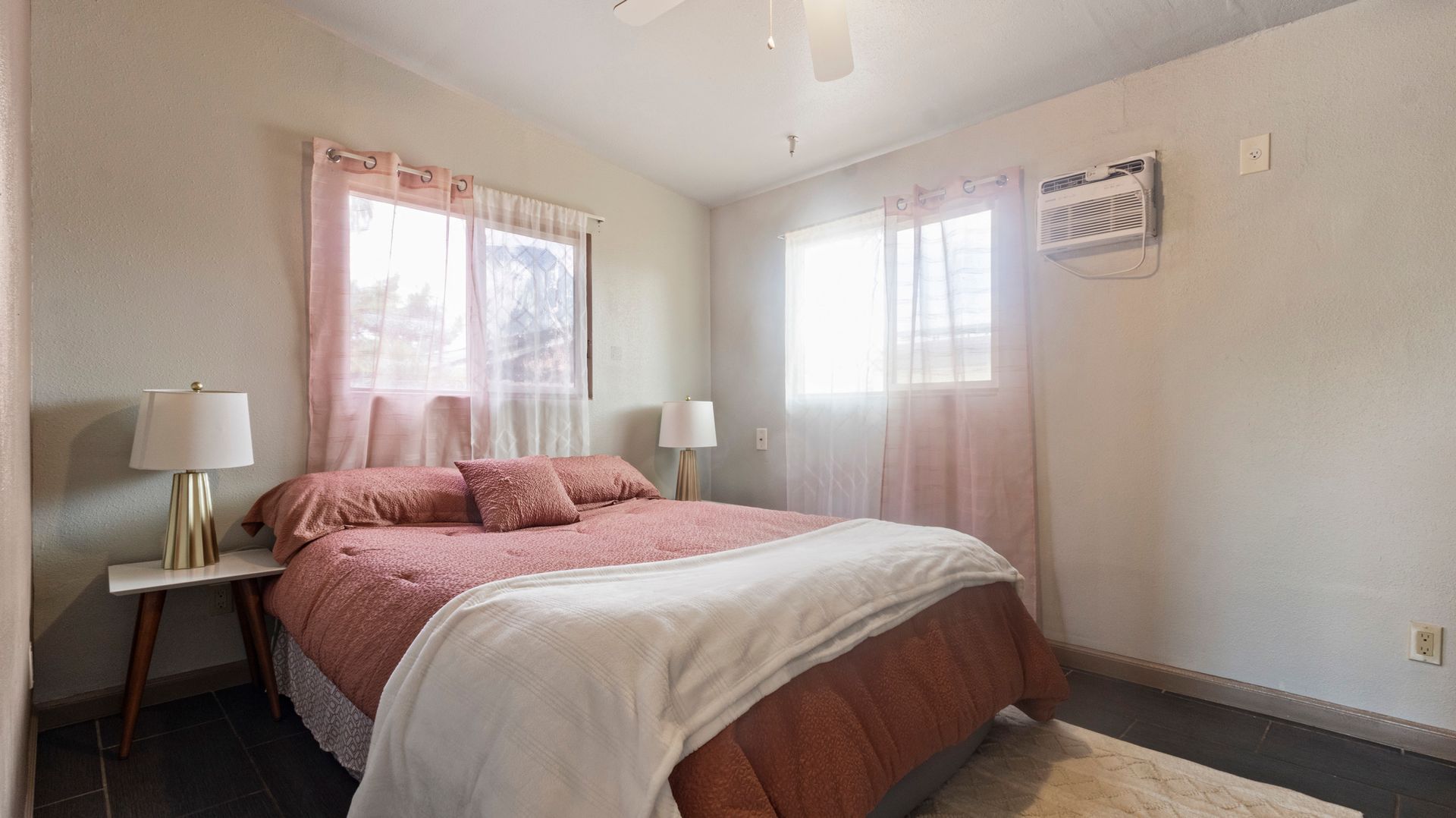 A bedroom with a bed , two lamps , and a window.