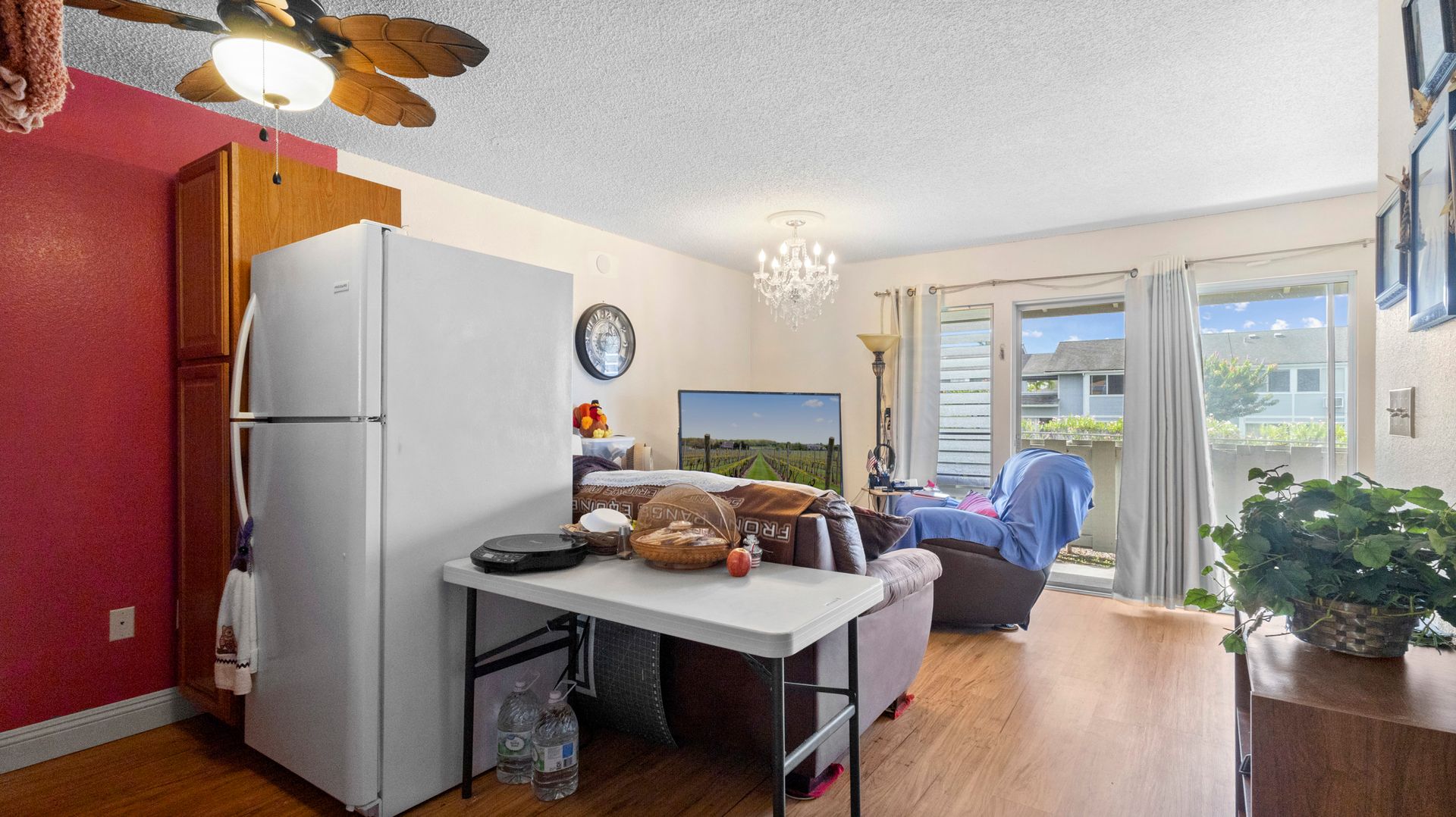 A living room with a table , refrigerator and ceiling fan.