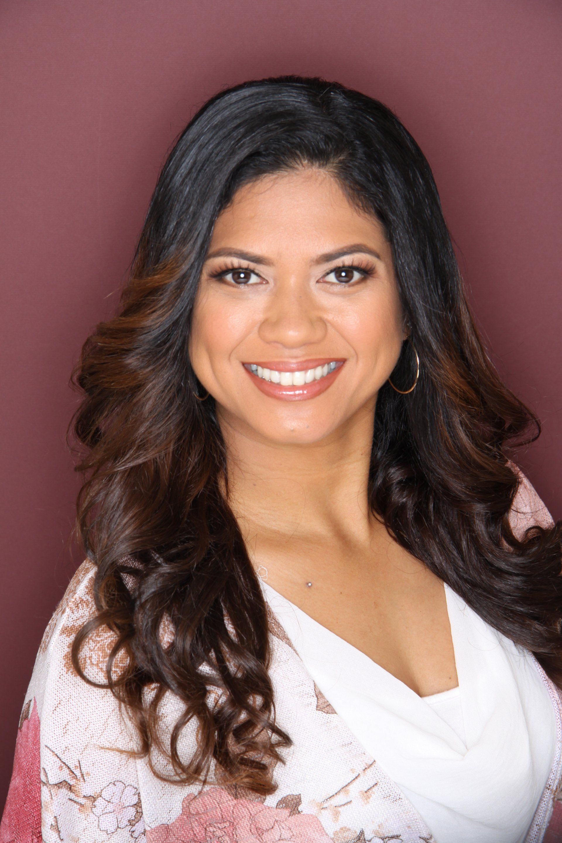 A woman with long hair and a white shirt is smiling for the camera.