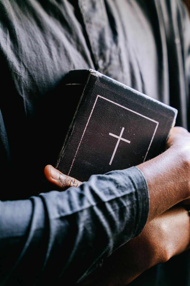 A man is holding a bible with a cross on the cover.
