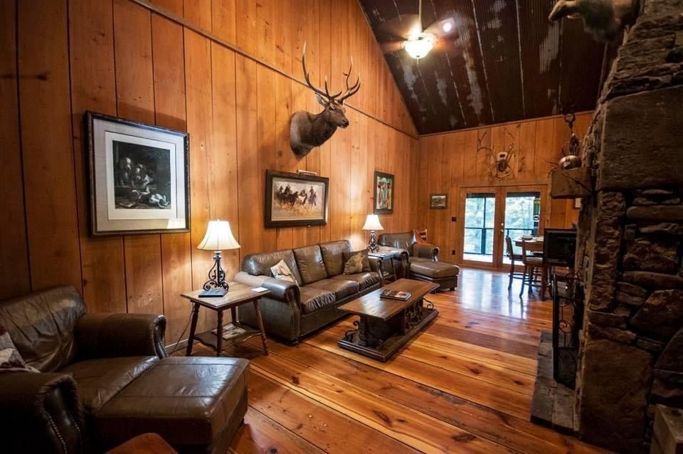 Cozy lodge living room with leather furniture, fireplace, wooden walls and floor, and mounted elk head.