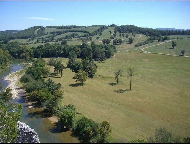 River and field landscape with green hills, trees, and blue sky.