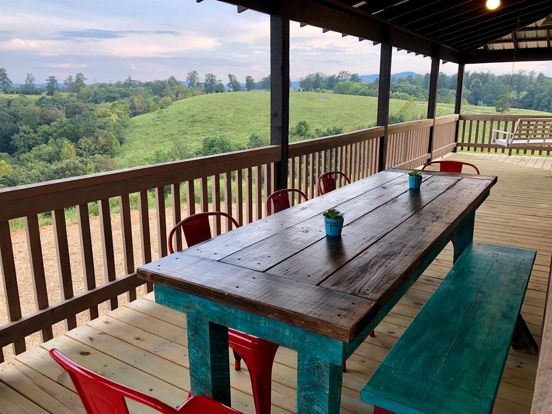 Wooden deck with table and chairs overlooking green hills and a cloudy sky.