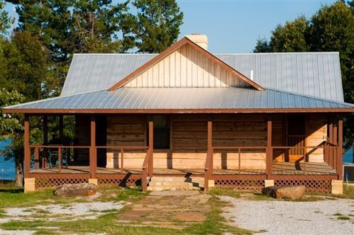 Log cabin with porch, metal roof, and chimney. Surrounded by trees and a dirt yard.