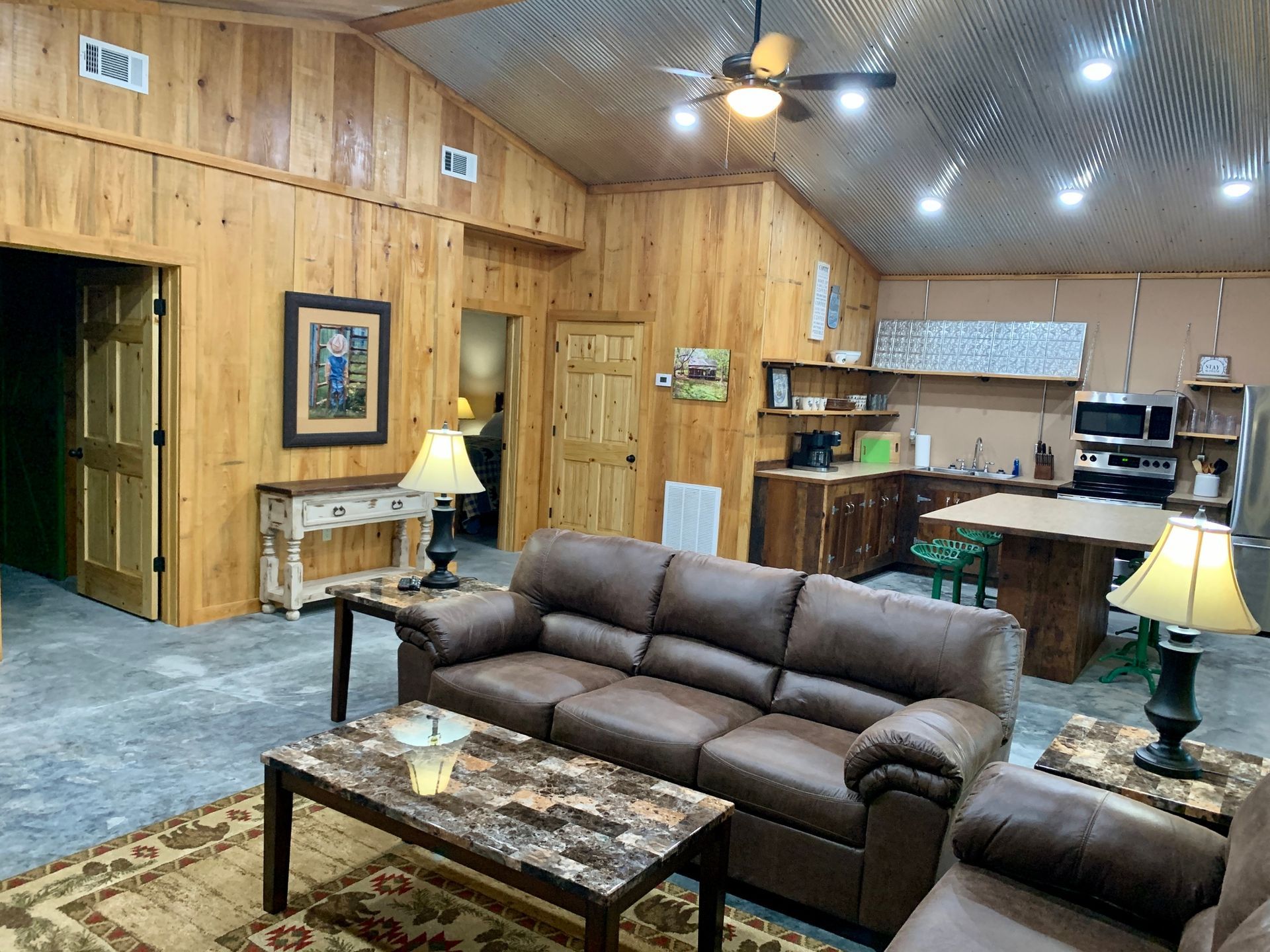 Living space with leather sofa, coffee table, kitchen, and wood paneling on walls.