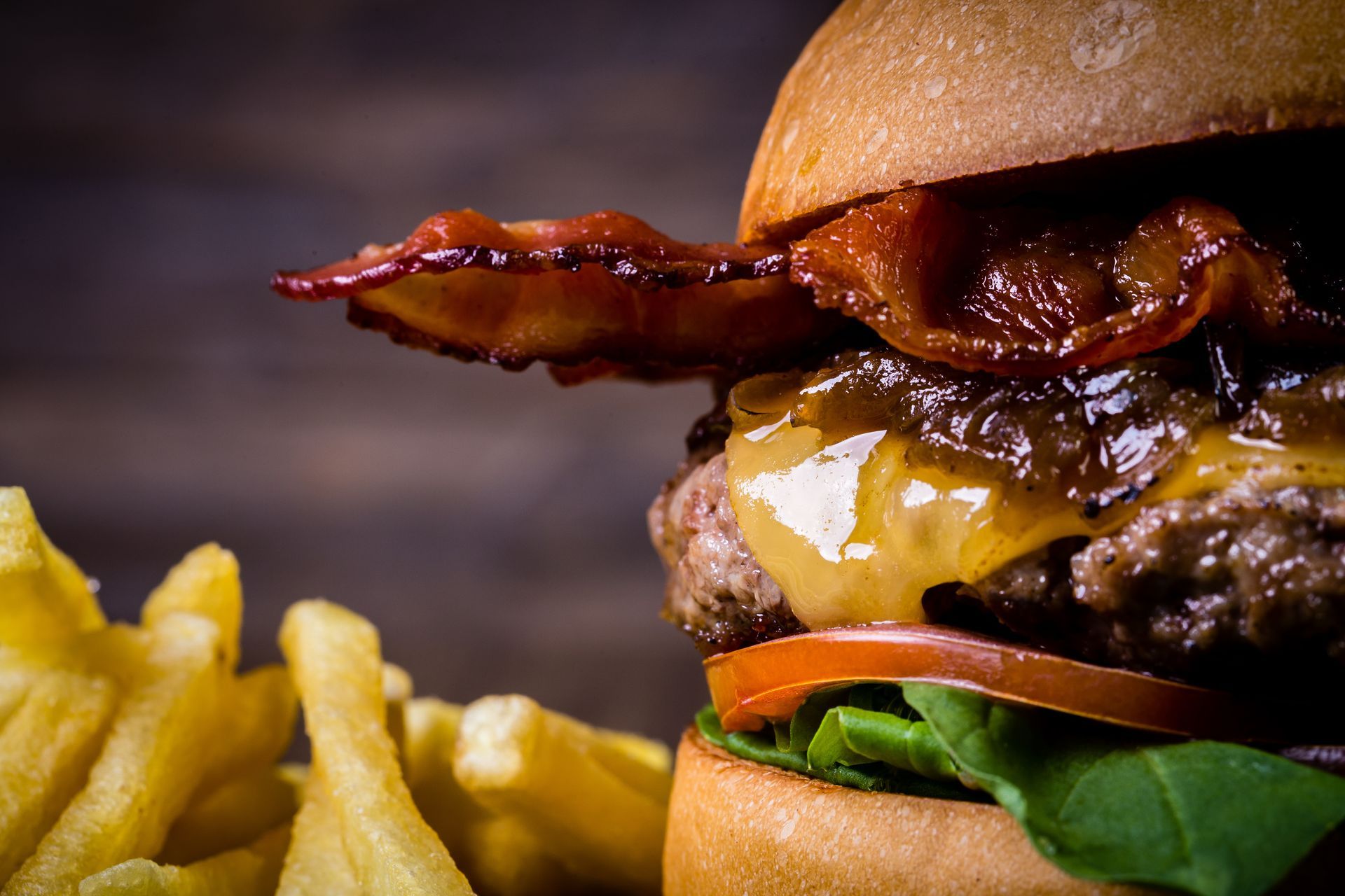Close-up of a bacon cheeseburger with fries on a wooden surface.