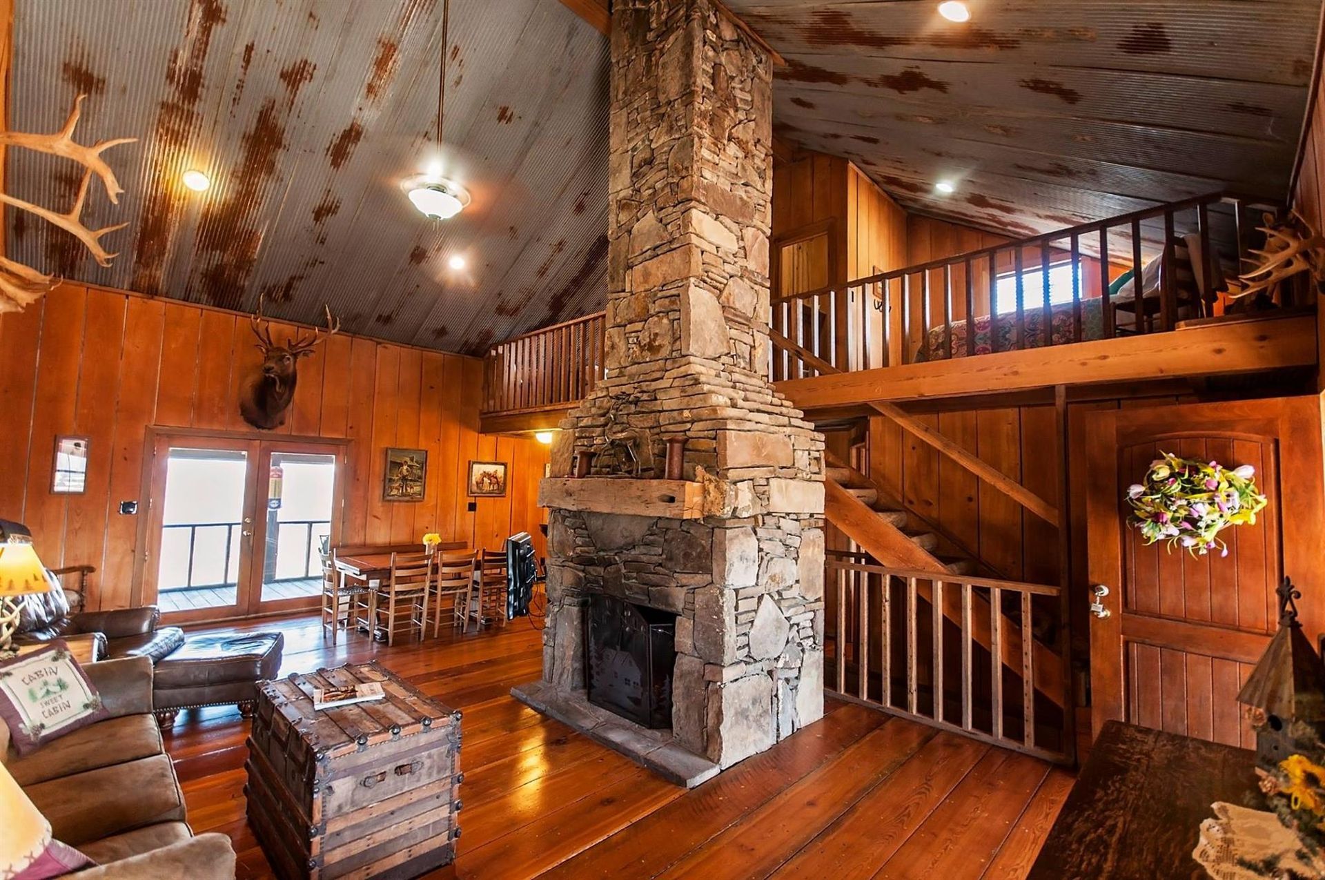 Rustic cabin interior with stone fireplace, wood paneling, and loft overlooking living area.