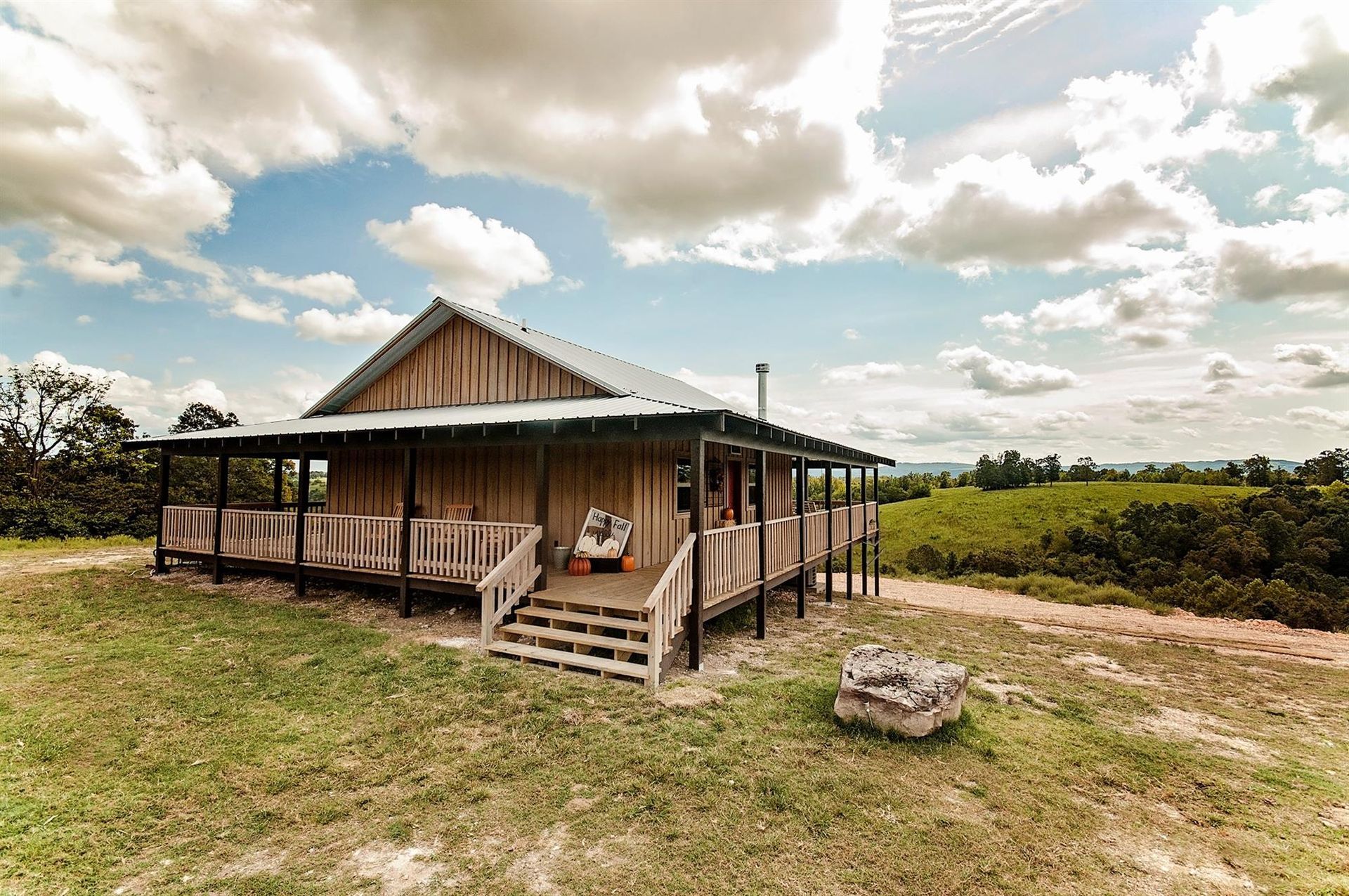 Wooden cabin with porch on a grassy hill, under a partly cloudy sky.