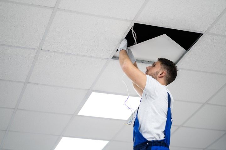 A man is fixing a light fixture on the ceiling.