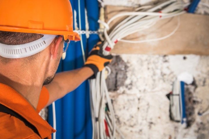 A man wearing a hard hat and gloves is working on electrical wires.