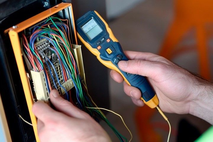 A person is holding a thermometer in front of a bunch of wires