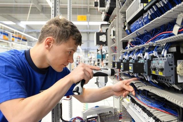 A man in a blue shirt is working on a machine in a factory.