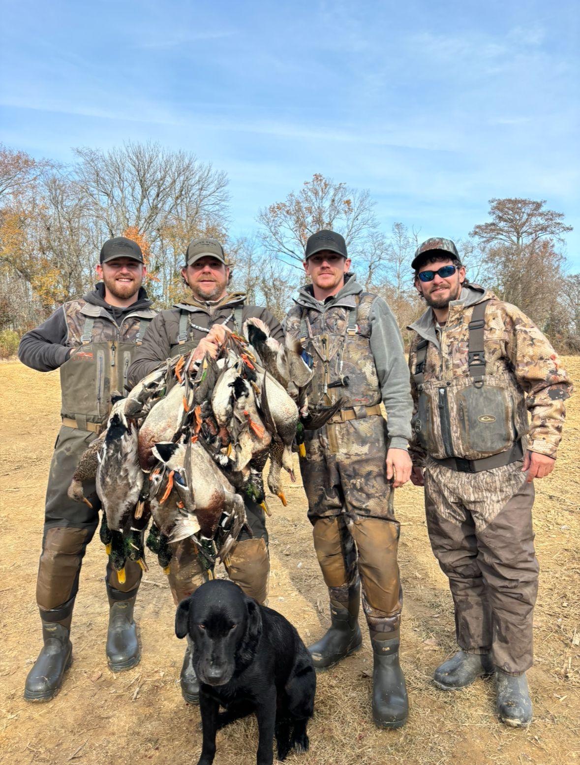 A group of men are standing next to each other holding ducks and a dog.