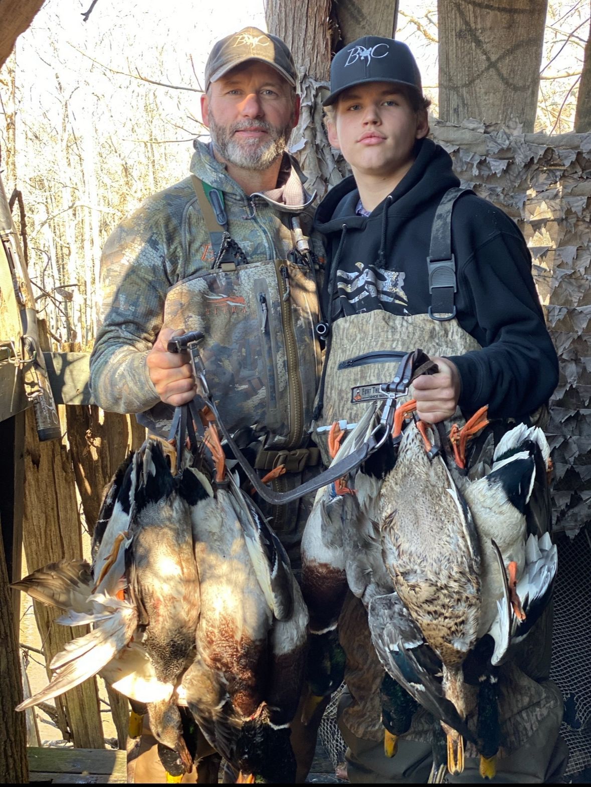 A man and a boy are standing next to each other holding ducks.