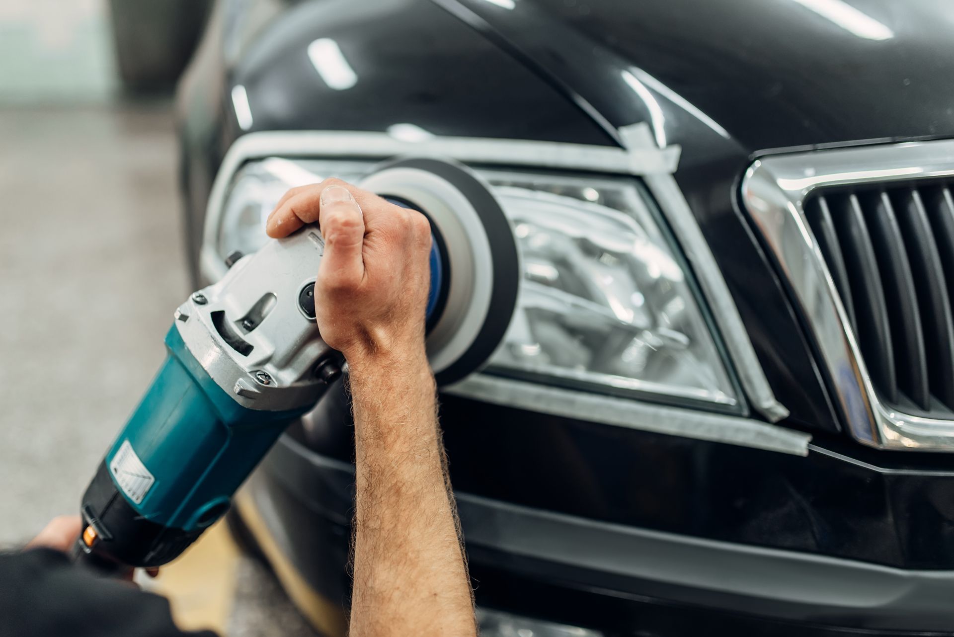 A man is polishing the headlights of a car with a machine